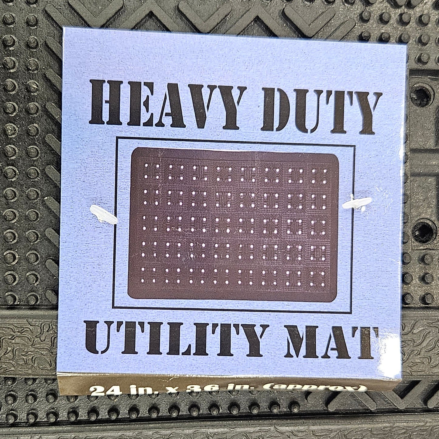 A square utility mat with a brown grid pattern and black text reading 'HEAVY DUTY MAT' on a light blue backing, shown attached to a textured dark gray industrial surface.