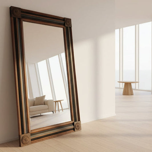 Large mirror with a wooden frame leaning against a white wall in a bright room.