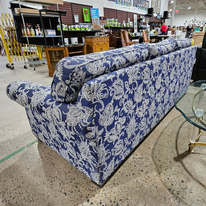 Blue patterned sofa in a store setting with a glass table on a speckled floor.