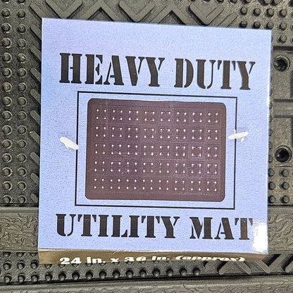 A square utility mat with a brown grid pattern and black text reading 'HEAVY DUTY MAT' on a light blue backing, shown attached to a textured dark gray industrial surface.