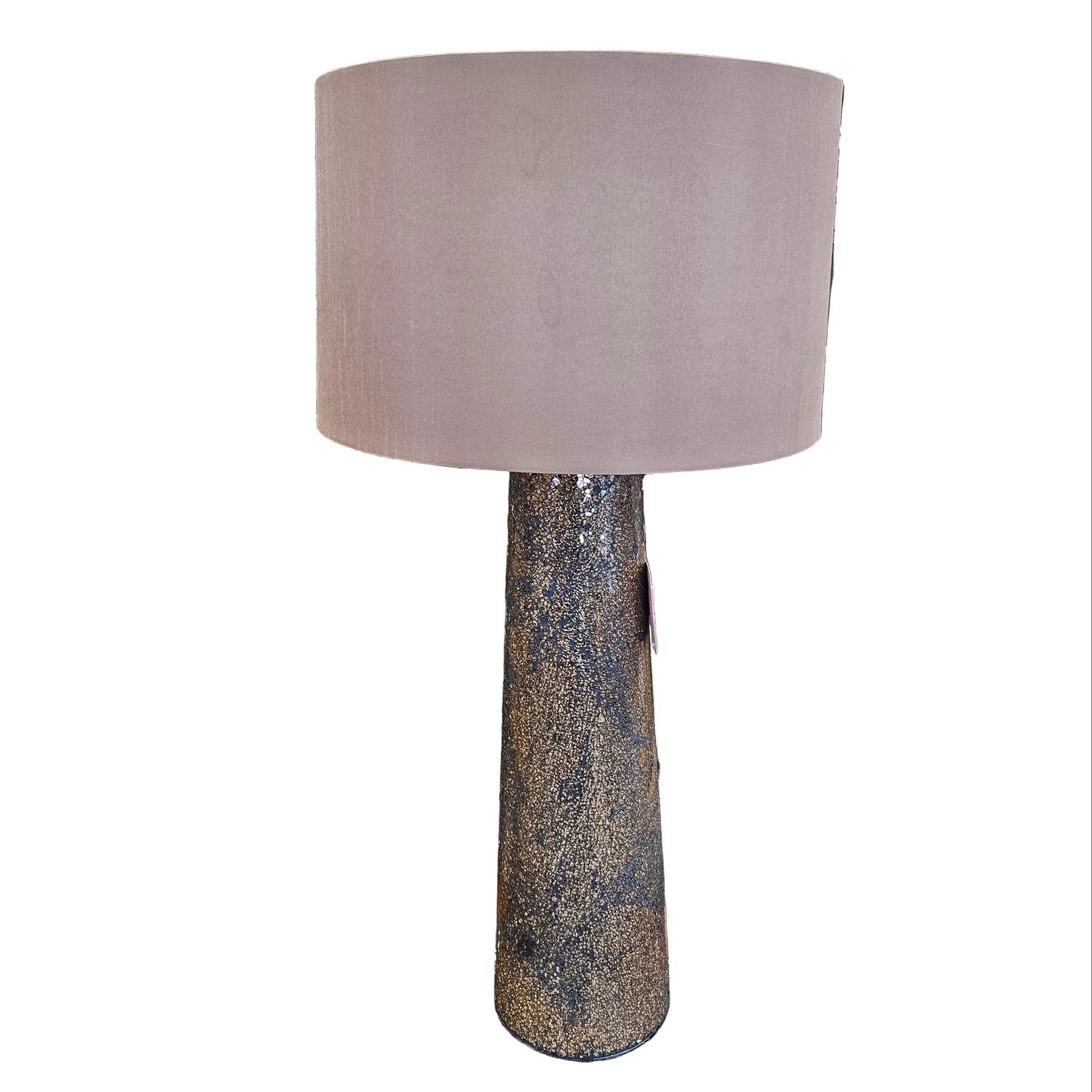 A table lamp with a large dusty pink fabric drum shade and a textured, speckled dark brown and gold base, shown in a cluttered furniture store setting.
